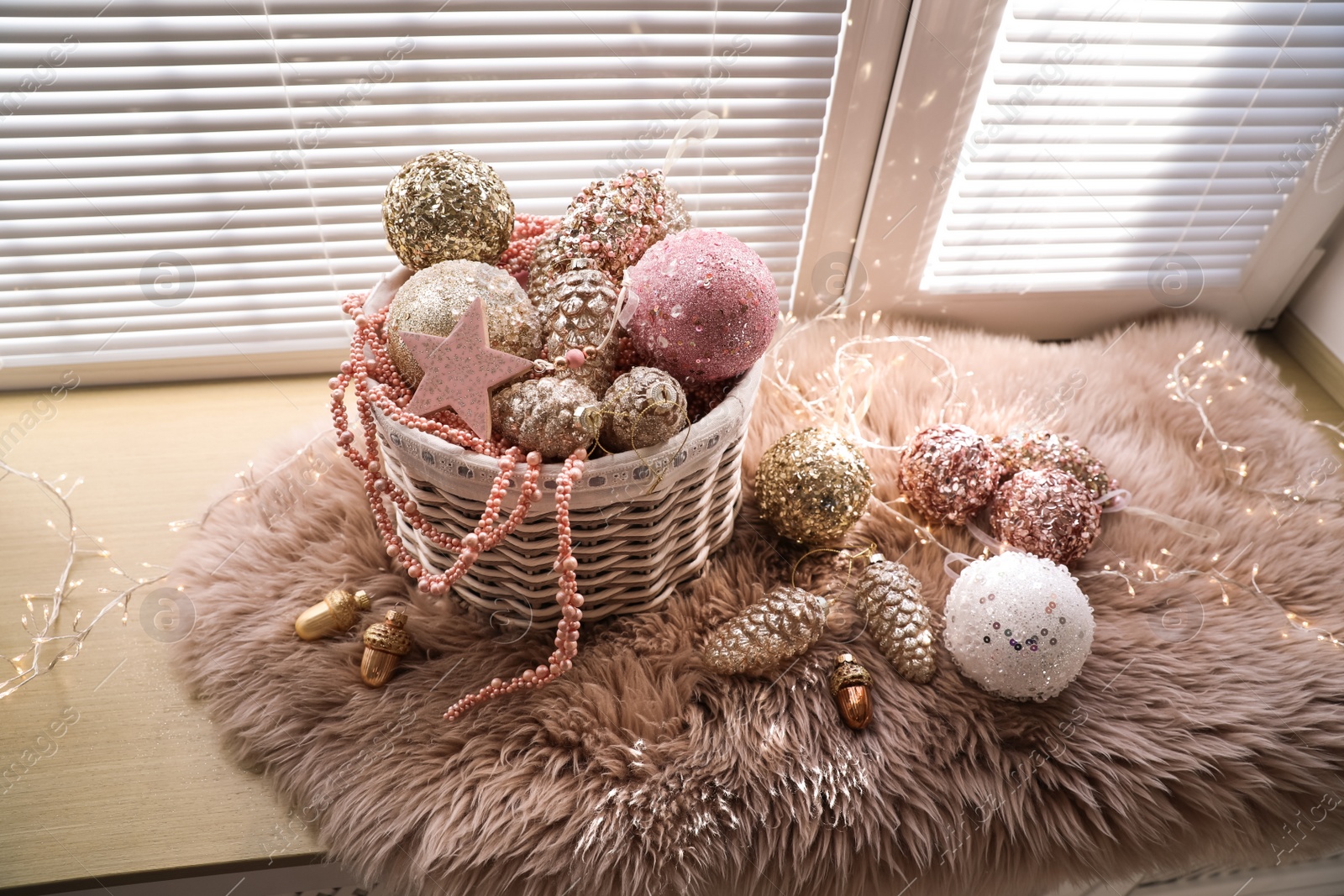 Photo of Basket with beautiful Christmas tree baubles and fairy lights on window sill indoors