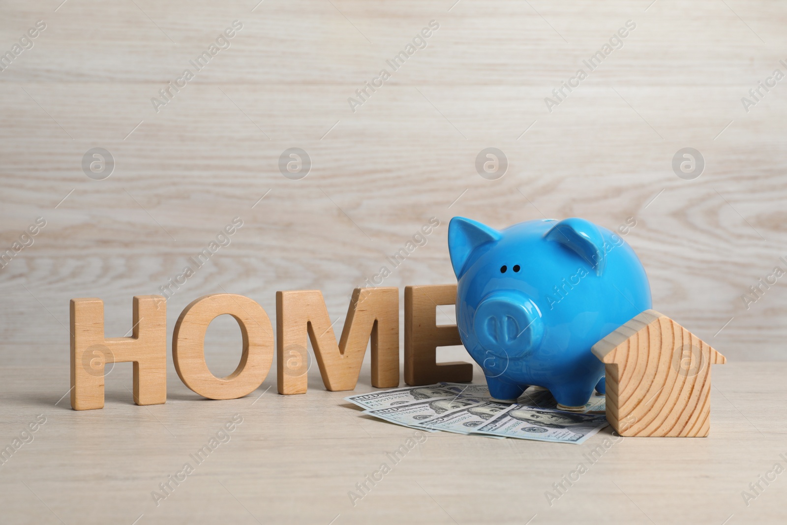 Photo of Piggy bank, house model, banknotes and word Home made of wooden letters on table
