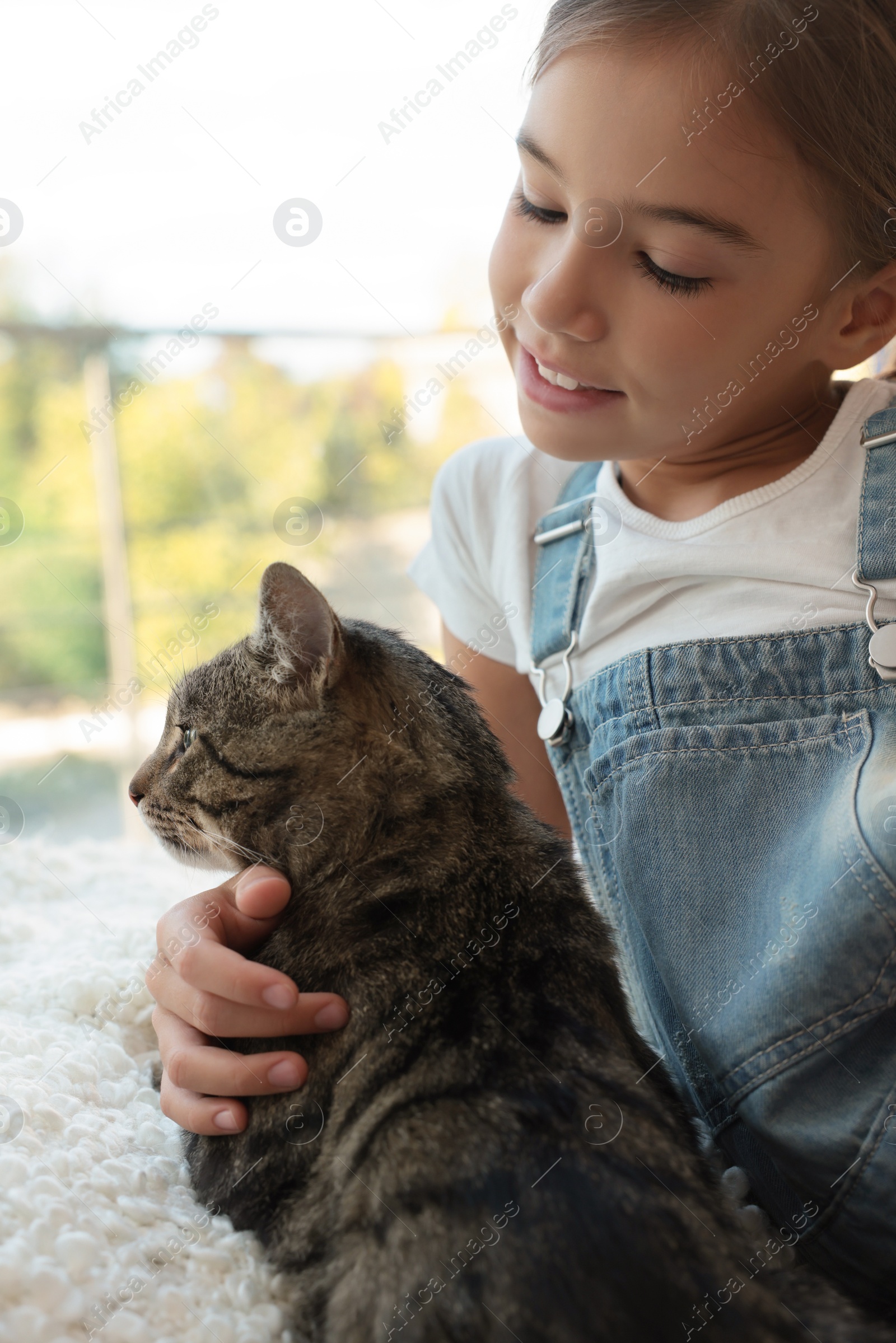 Photo of Cute little girl with her cat near window at home. Childhood pet