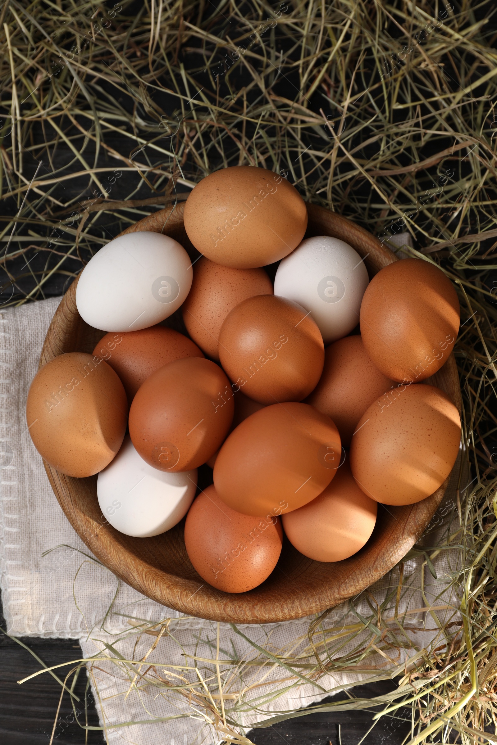 Photo of Fresh chicken eggs in bowl and dried hay on black wooden table, flat lay