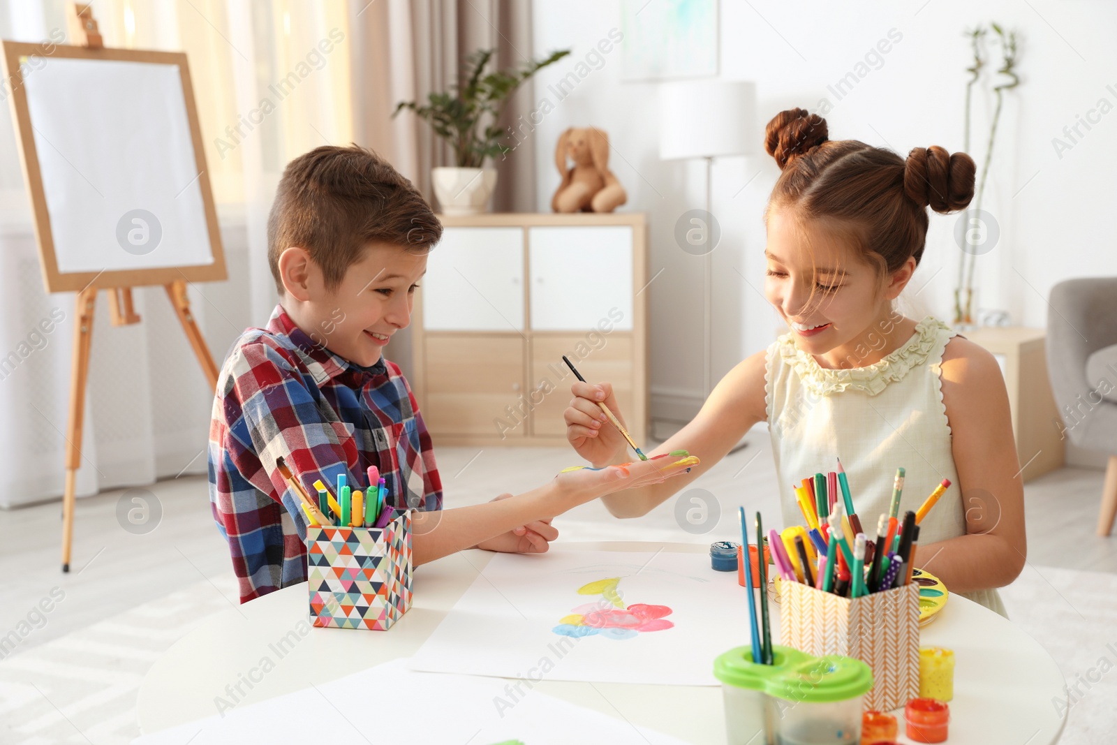 Photo of Little children painting hands at table indoors