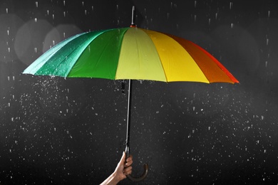 Photo of Woman holding bright umbrella under rain on dark background, closeup