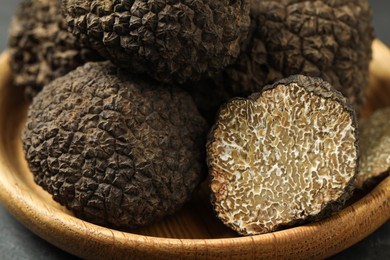 Photo of Whole and cut black truffles on wooden plate, closeup