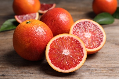 Photo of Whole and cut red oranges on wooden table, closeup