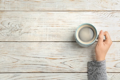 Photo of Young woman with cup of delicious hot coffee on wooden background, top view