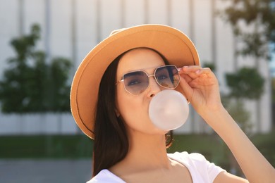 Photo of Beautiful woman in stylish sunglasses blowing gum outdoors on sunny day