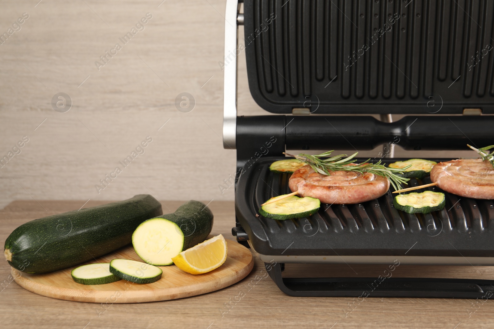 Photo of Electric grill with homemade sausages, zucchini and rosemary on wooden table