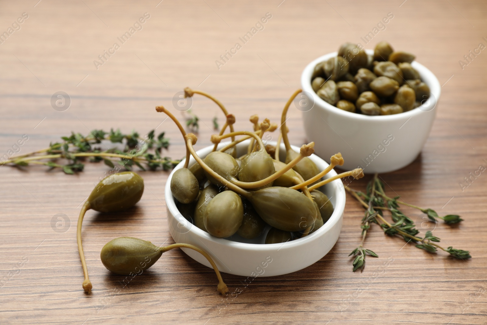 Photo of Delicious pickled capers and thyme twigs on wooden table