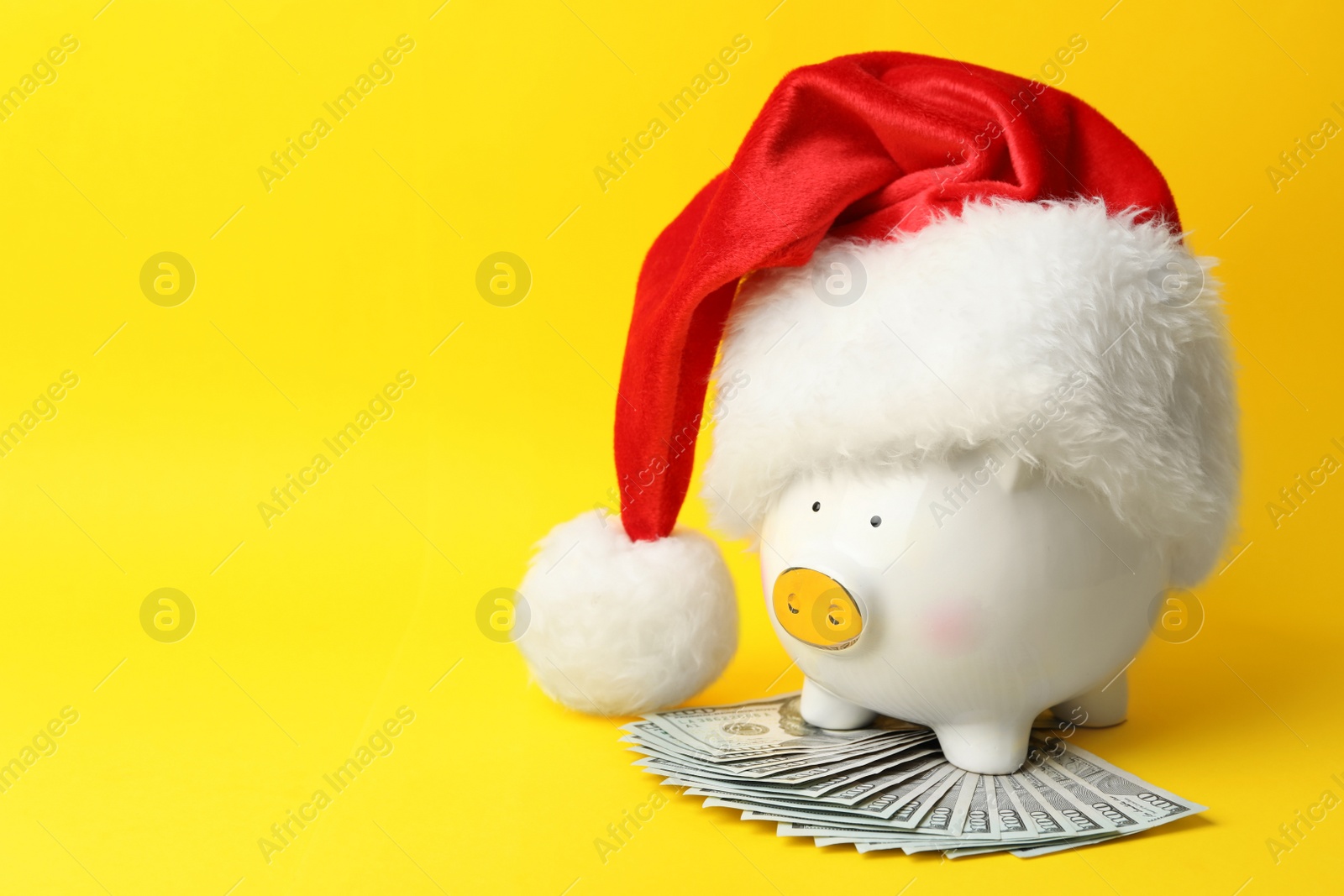 Photo of Piggy bank with Santa hat and dollar banknotes on yellow background. Space for text