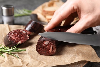 Photo of Woman cutting tasty blood sausage at table, closeup
