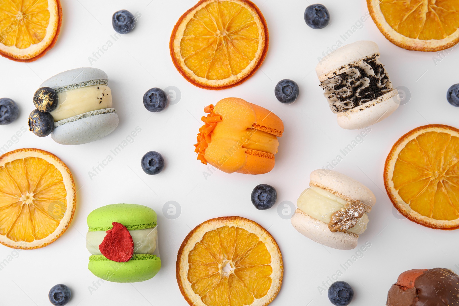 Photo of Delicious macarons, dry orange slices and blueberries on white table, flat lay