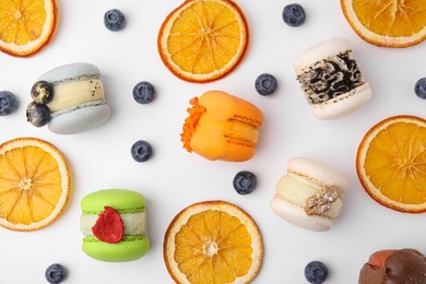 Delicious macarons, dry orange slices and blueberries on white table, flat lay