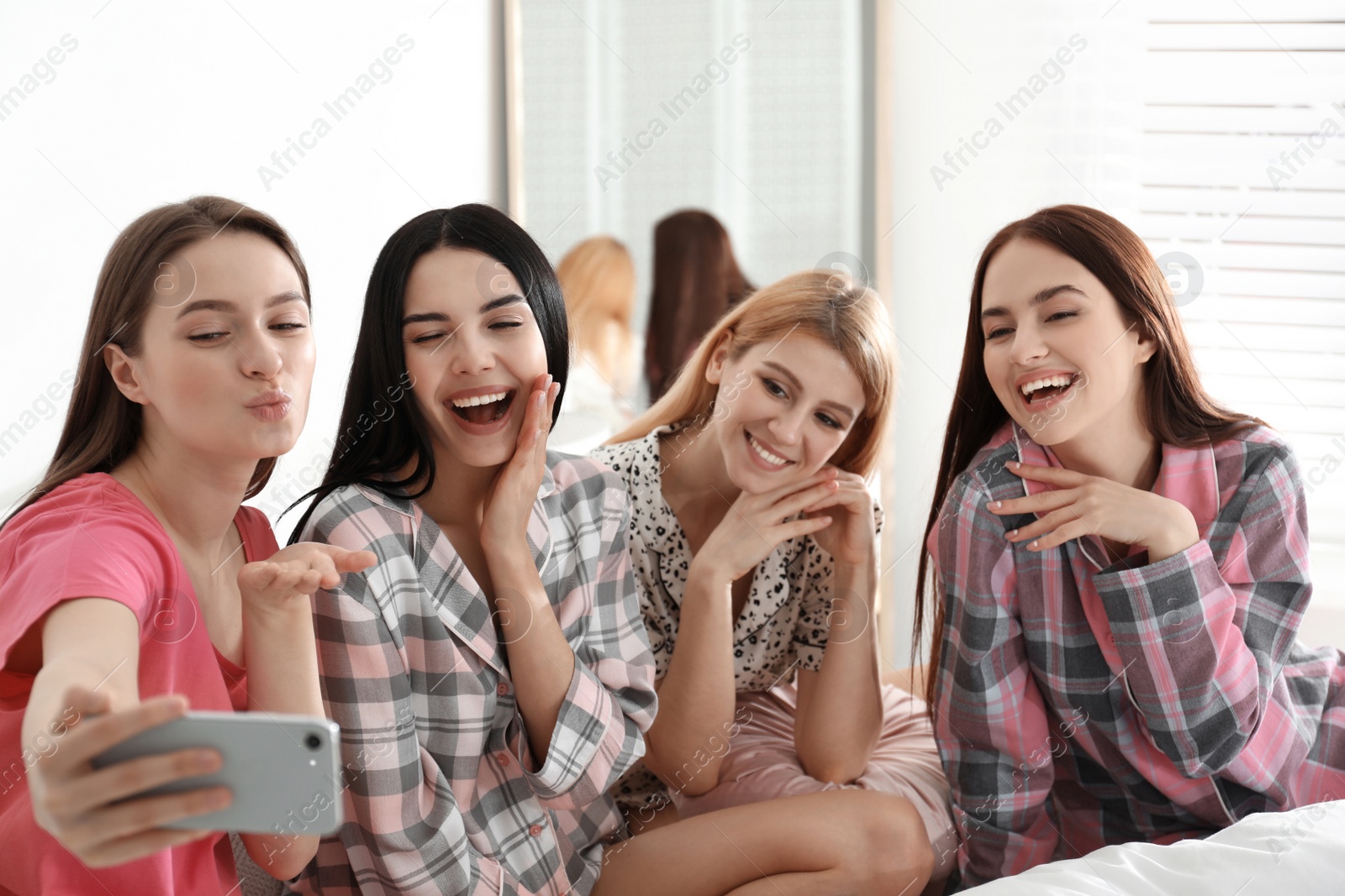 Photo of Beautiful young ladies taking selfie on bed at pamper party. Women's Day