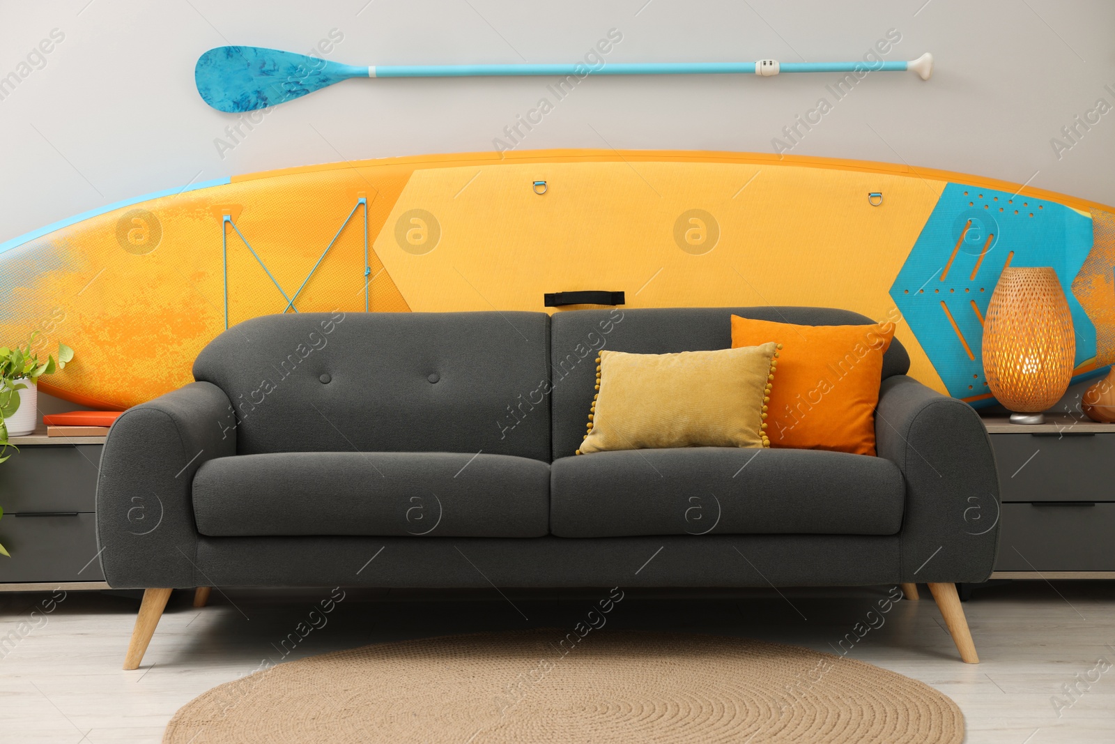 Photo of SUP board, paddle and stylish sofa in living room. Interior design