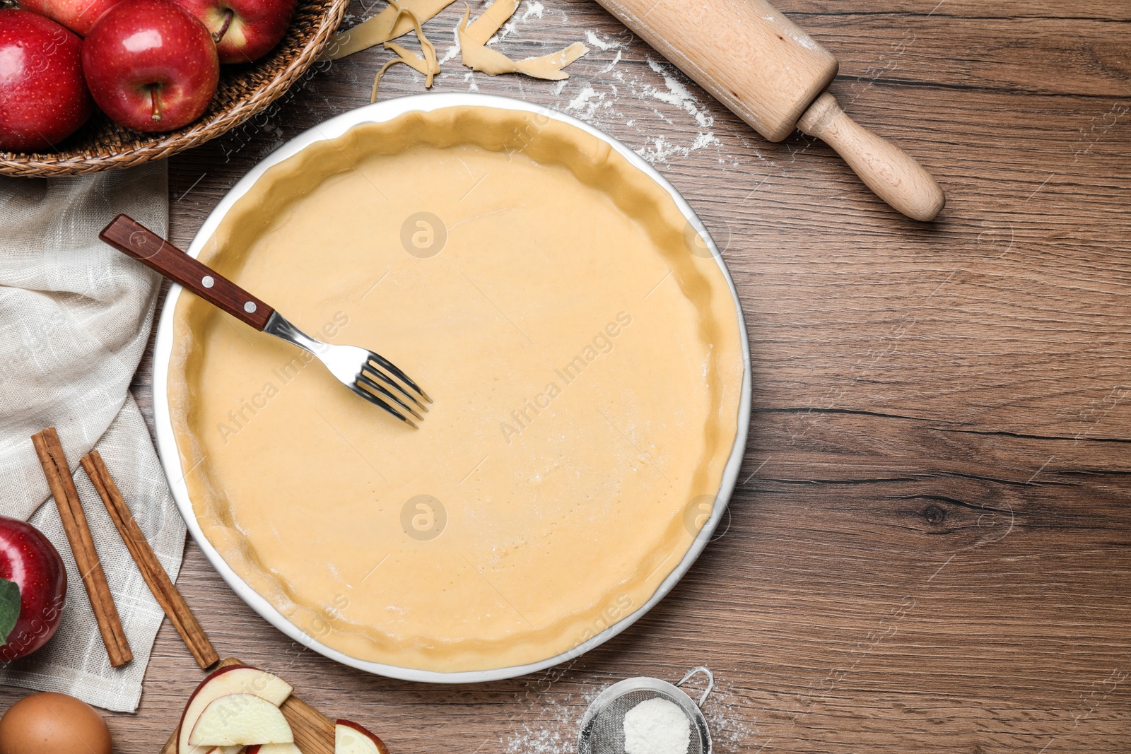 Photo of Flat lay composition with raw dough, fork and ingredients on wooden table, space for text. Baking apple pie