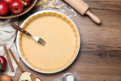 Flat lay composition with raw dough, fork and ingredients on wooden table, space for text. Baking apple pie