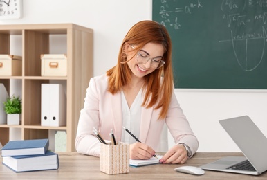 Photo of Beautiful young teacher working at table in classroom