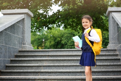 Photo of Cute school child with stationery near stairs in park