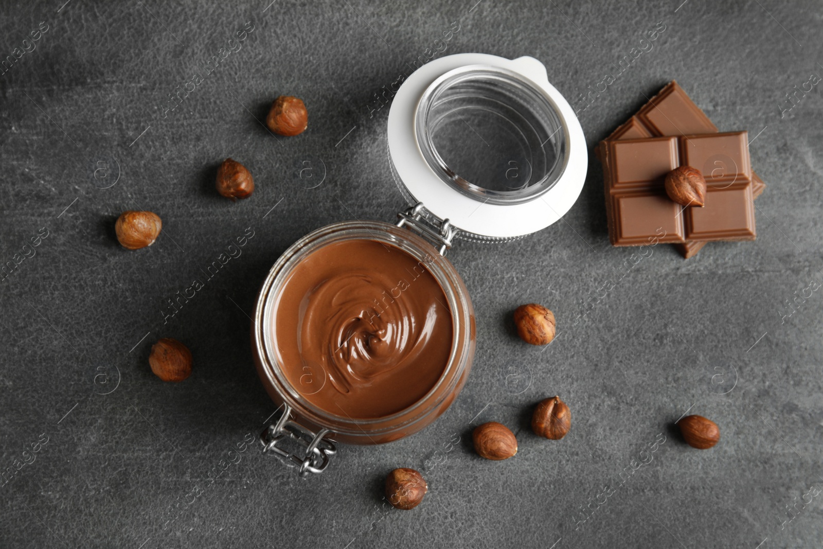 Photo of Flat lay composition with tasty chocolate cream in glass jar and hazelnuts on table