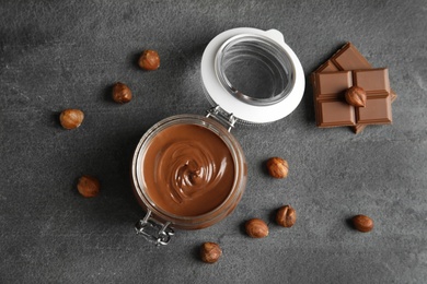 Flat lay composition with tasty chocolate cream in glass jar and hazelnuts on table