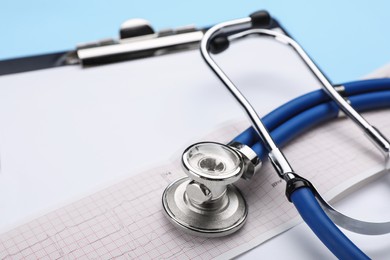 Stethoscope, clipboard and cardiogram paper on light blue background, closeup