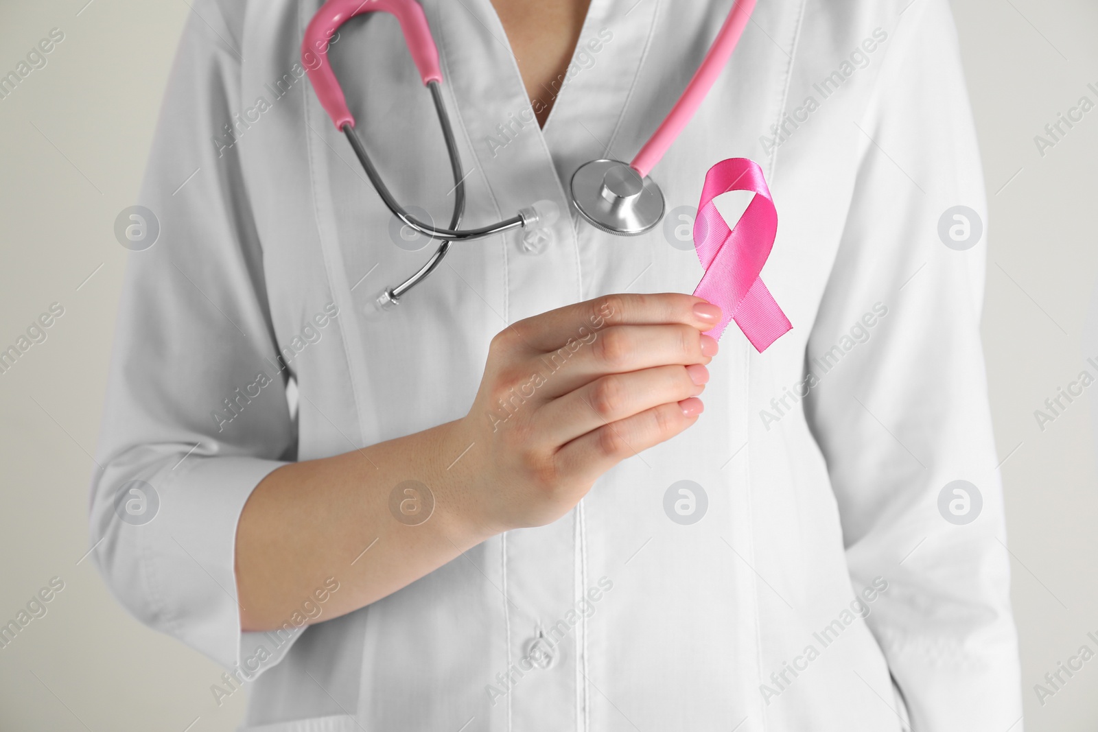 Photo of Mammologist with pink ribbon on light background, closeup. Breast cancer awareness