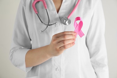 Photo of Mammologist with pink ribbon on light background, closeup. Breast cancer awareness