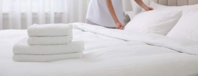 Image of Chambermaid making bed in hotel room, focus on fresh towels. Banner design