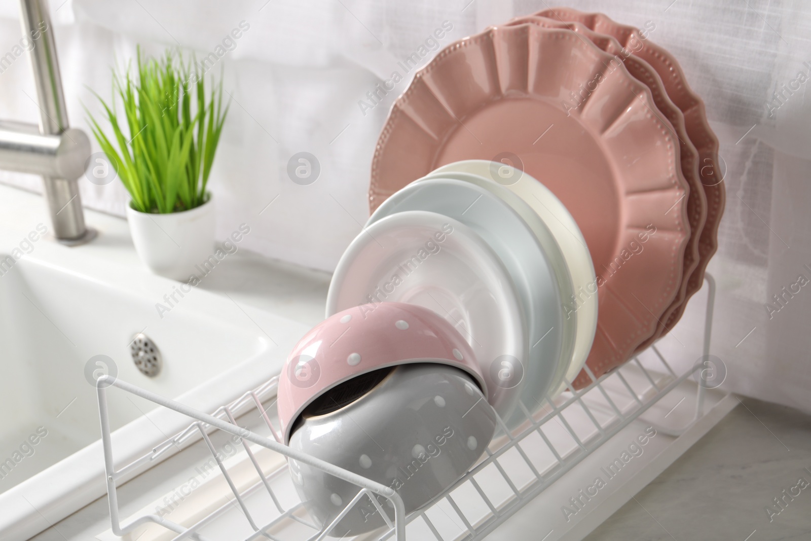 Photo of Drainer with different clean dishware on white table in kitchen