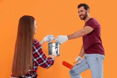 Photo of Man taking can of paint from woman near orange wall. Interior design