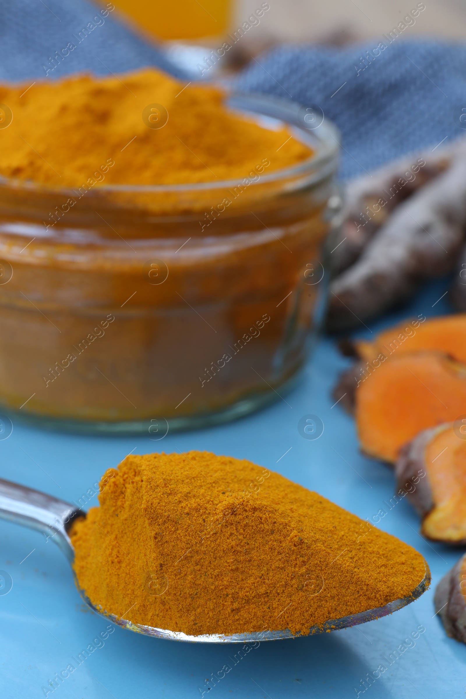 Photo of Glass jar of turmeric powder and roots on light blue tray, closeup