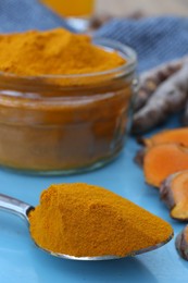 Glass jar of turmeric powder and roots on light blue tray, closeup