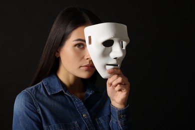 Photo of Multiple personality concept. Woman with mask on black background, space for text