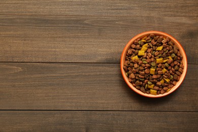 Photo of Dry food in pet bowl on wooden background, top view. Space for text