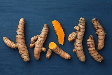 Whole and cut turmeric roots on blue wooden table, flat lay