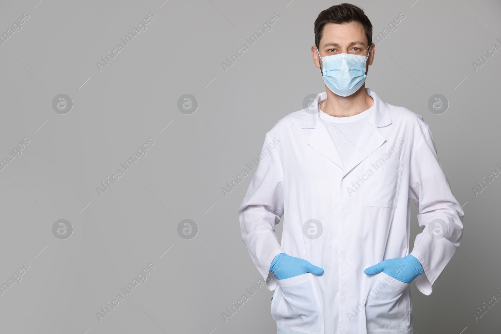 Photo of Doctor or medical assistant (male nurse) in uniform with protective mask on light grey background. Space for text