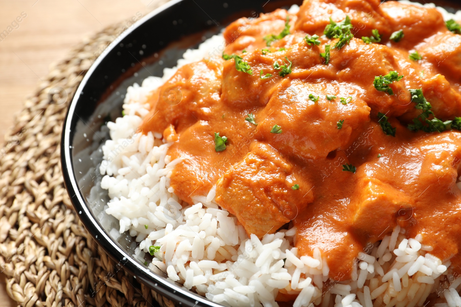 Photo of Delicious butter chicken with rice in dish on wooden table, closeup