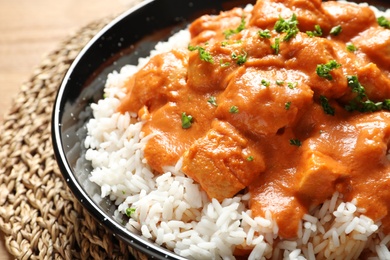 Delicious butter chicken with rice in dish on wooden table, closeup