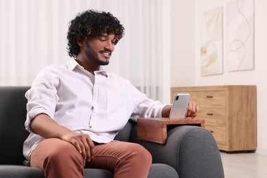Photo of Happy man using smartphone on sofa armrest wooden table at home