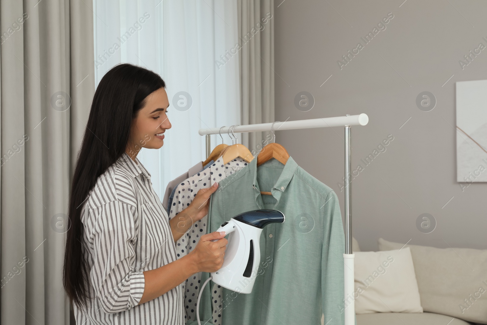 Photo of Woman steaming shirt on hanger at home