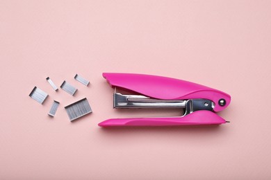 Photo of New bright stapler with staples on pink background, fat lay. School stationery