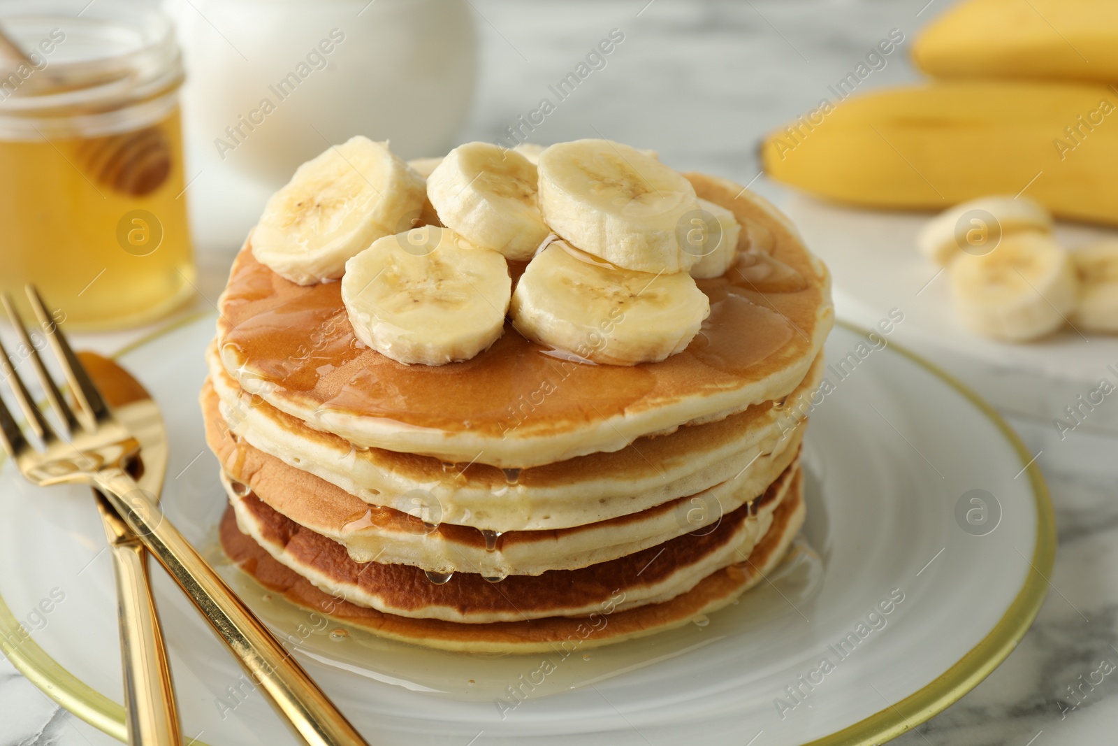 Photo of Delicious pancakes with bananas and honey on white marble table, closeup