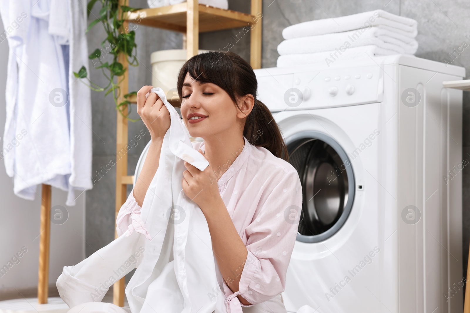 Photo of Young housewife with laundry near washing machine at home