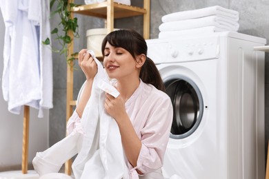 Young housewife with laundry near washing machine at home