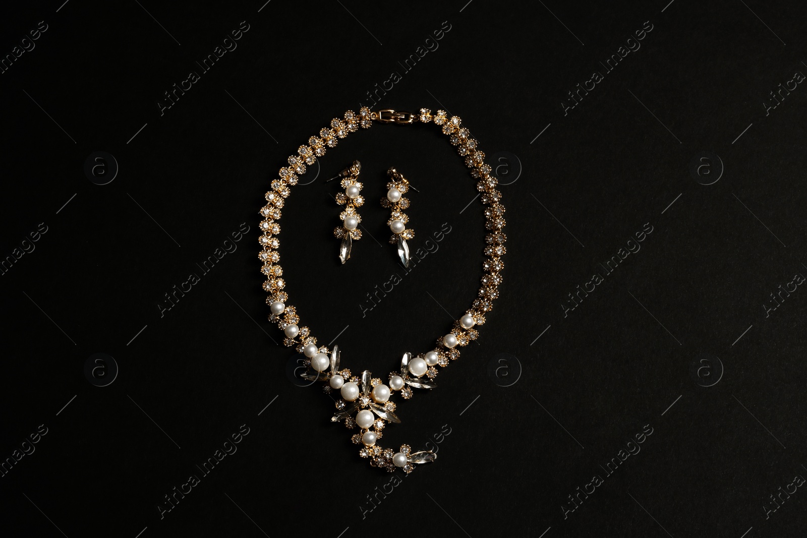 Photo of Set of elegant necklace and earrings on black background, top view. Luxury jewelry
