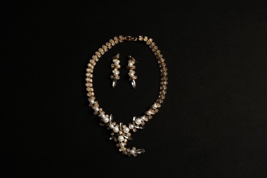 Set of elegant necklace and earrings on black background, top view. Luxury jewelry