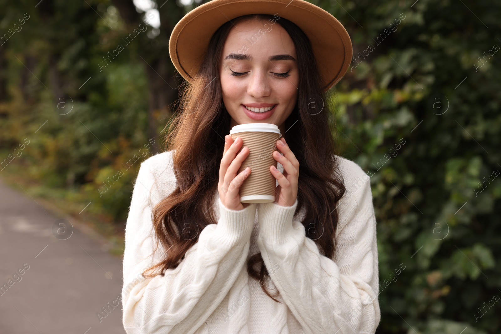 Photo of Beautiful young woman in stylish warm sweater holding paper cup of coffee outdoors