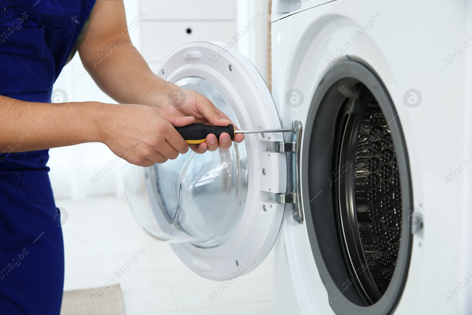 Photo of Young handyman fixing washing machine, closeup. Laundry day