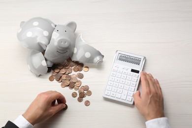Money savings. Businessman calculating coins from broken piggy bank at light wooden table, top view
