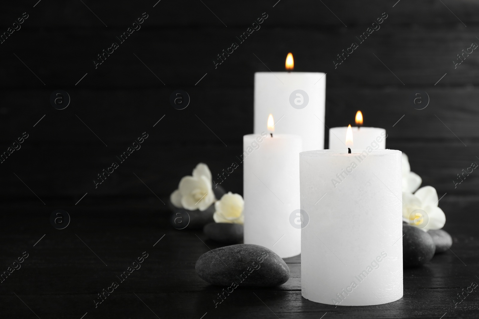 Photo of Burning candles, spa stones and flowers on table. Space for text